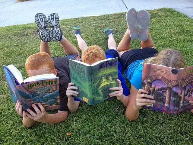 Three kids laying on the grass reading Harry Potter books.